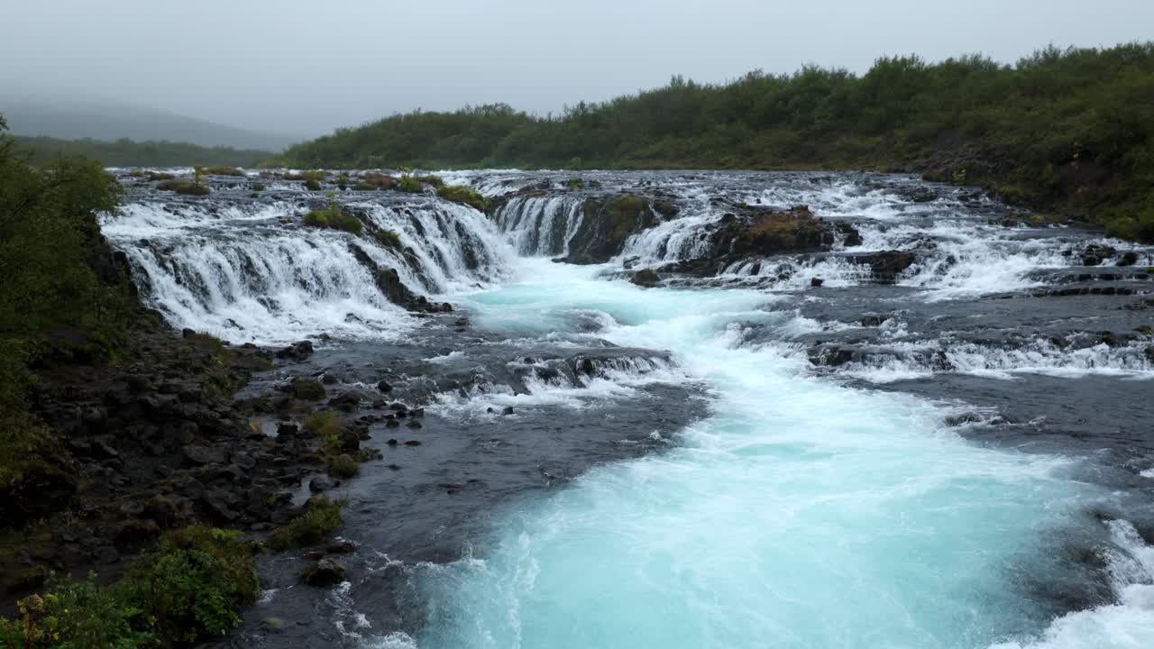 río con una cascada muy grande y poderosa cerca del bosque y entre las rocas negras en un día nublado