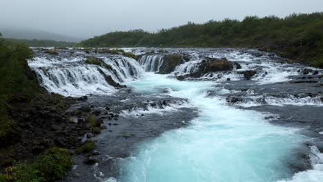 river with a very big and mighty waterfall near the forest and between the black rocks on a cloudy day