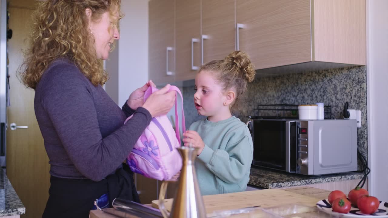 Mother helping her daughter with her jacket in the kitchen