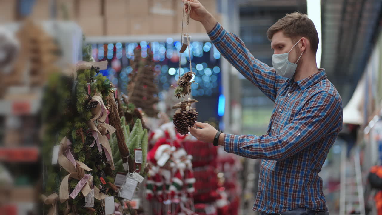 compras en pandemia y cuarentena. un hombre con una máscara protectora en una joyería y guirnaldas con juguetes para árboles de navidad y en casa. guirnaldas navideñas y decoración.