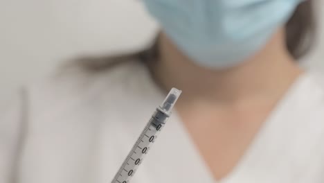 close-up of a female healthcare worker wearing gloves removing a needle from a vaccine syringe