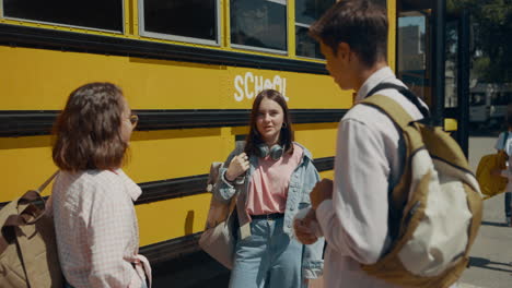 Students-standing-together-talking-at-school-bus.-Teen-schoolchildren-chatting.