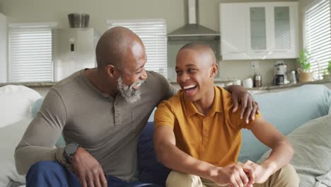 video of happy african american father and son sitting on sofa and laughing