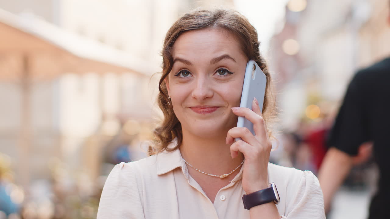 Happy young woman having remote conversation talking on smartphone good news gossip in city street