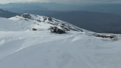 Snow-groomer-parked-on-top-of-snowy-peak,-a-second-snow-groomer-driving-up