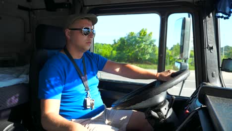 driver in sunglasses sitting behind steering wheel of his truck and riding on country road at sunny day. man controlling his truck attentive watching road. trucker inside car. slow motion close up