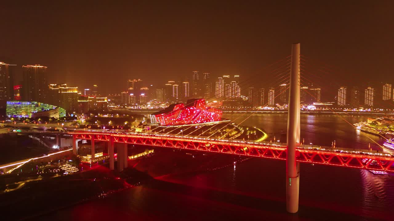 A vibrant night scene of a bridge in Chongqing, China, with a theater structure lit up in red. The city skyline gleams in the background, showcasing the city's modern architecture and dynamic energy.