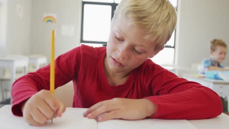 Video-of-happy-caucasian-boy-sitting-at-school-desk-and-writing