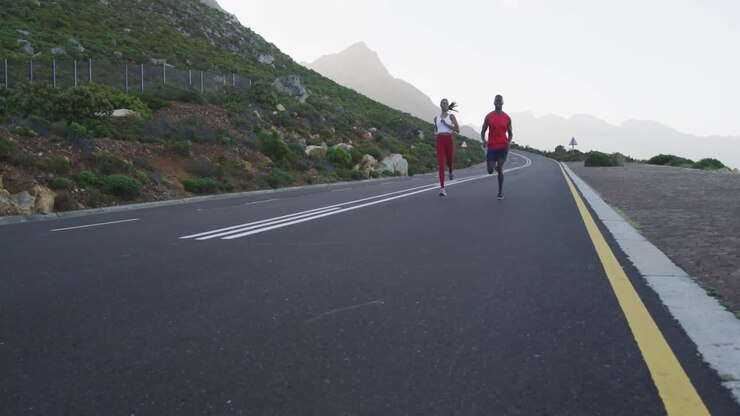 Coppia in forma e multietnica che corre su una strada di campagna vicino alle montagne