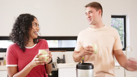 smiling young multiracial couple enjoying green smoothies together in modern kitchen, at home