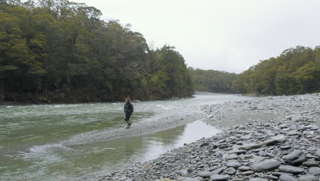 woman in hiking gear walking alongside river in a valley on new zealand's south island