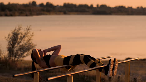 abdominal muscles exercises. a young beauty athletic at sunset against the lake in summer woman in sportswear doing exercises for abs in slow motion on the bar