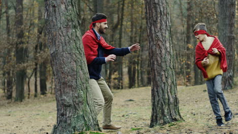 padre e hijo caucásicos alegres con capas rojas corriendo en el bosque y jugando a ser superhéroes