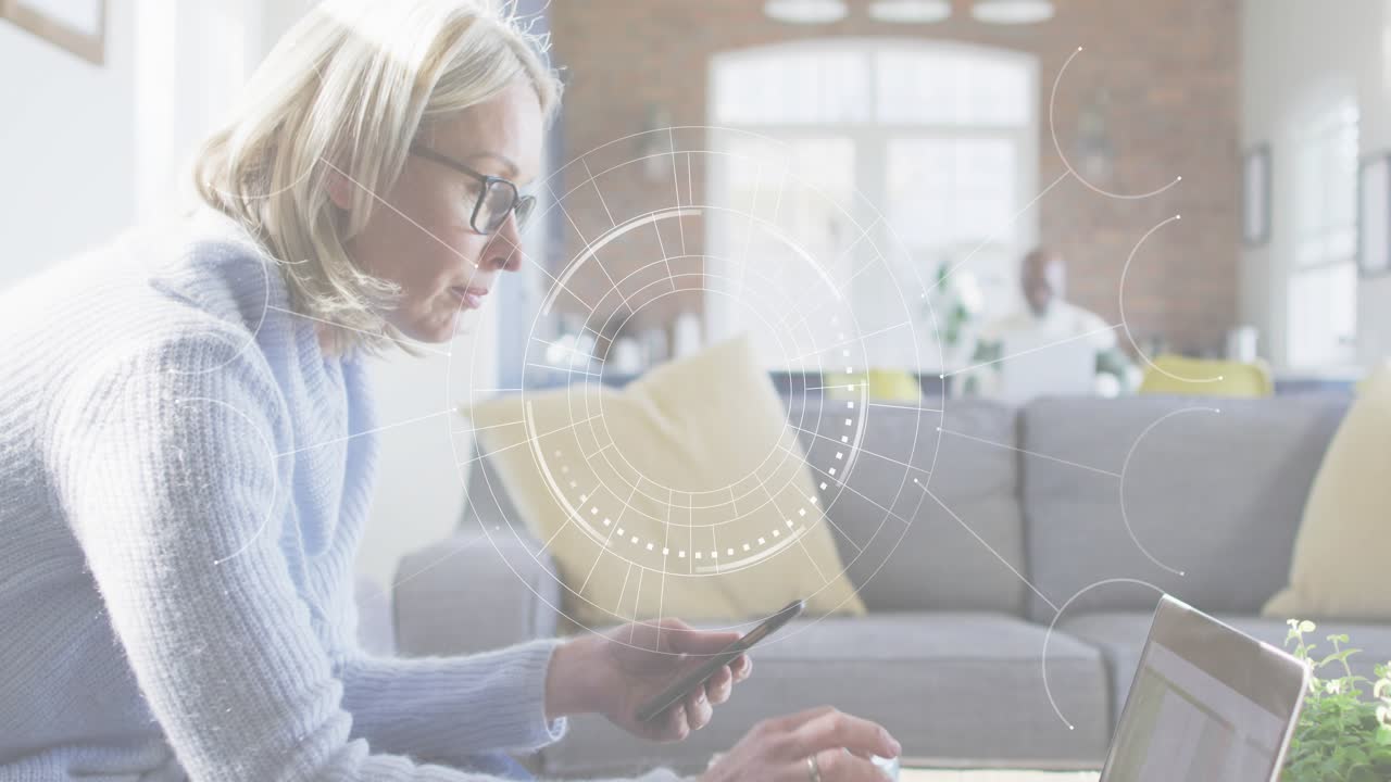 Woman shifting bill aside, tapping phone confirming payment, typing on laptop as UI graphic pulses