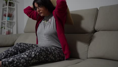 pregnant woman touching her belly and getting comfortable on the sofa
