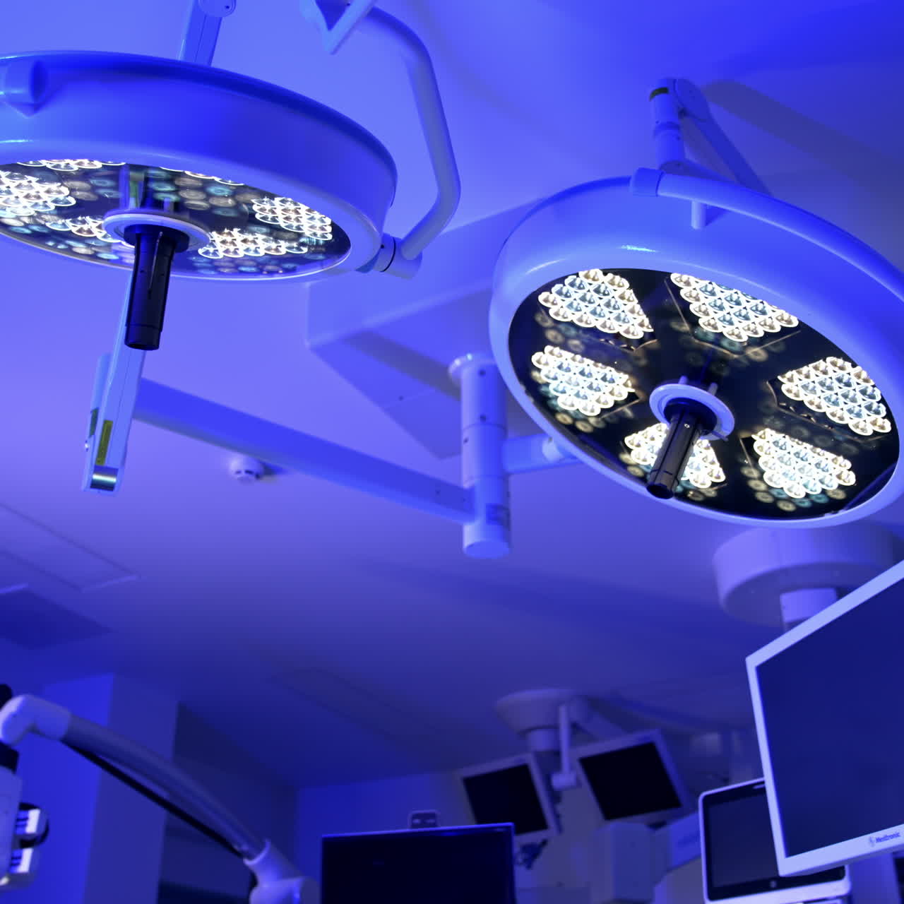 Dos lámparas redondas encendidas en el techo de un quirófano. Iluminación azul en la sala con equipo moderno. Vista en ángulo bajo.