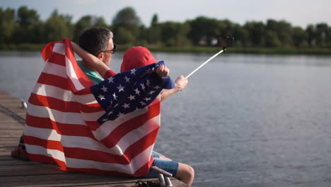 father and son taking a selfie with an american flag on a pier