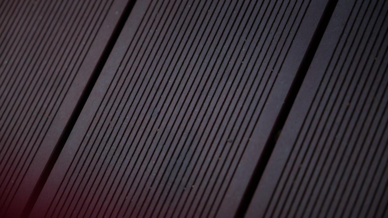 Detailní filmový záběr tmavých dřevěných terasových prken s lineárními drážkami a geometrickými vzory.