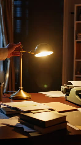 hand adjusting a vintage desk lamp on a cluttered desk with a typewriter