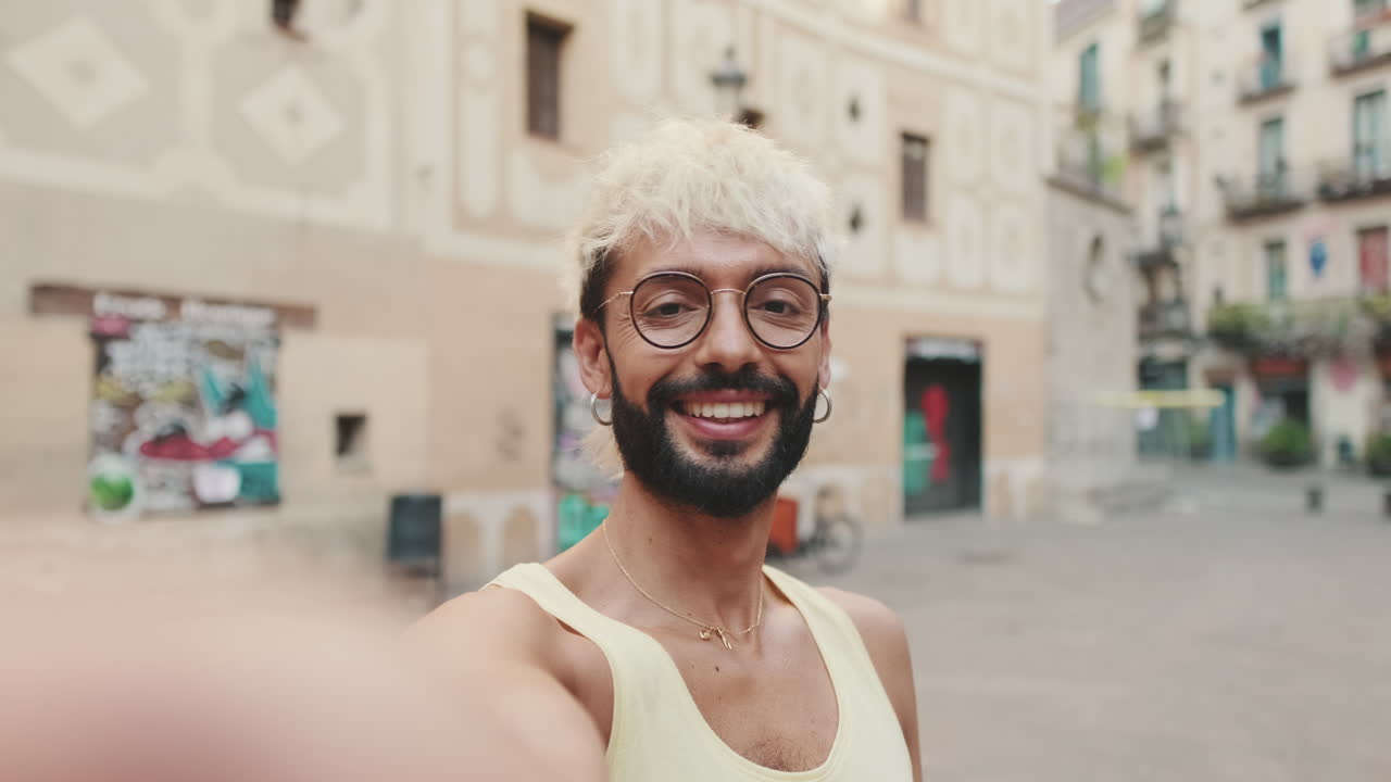 Giovane sorridente con gli occhiali che si fa un video selfie all'aperto
