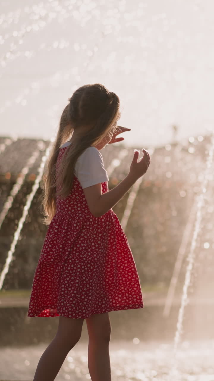 Little boy eats sugar candy wool with elder sister cooling down by fountain at sunset slow motion. Children with snack rest in city park. Summer time