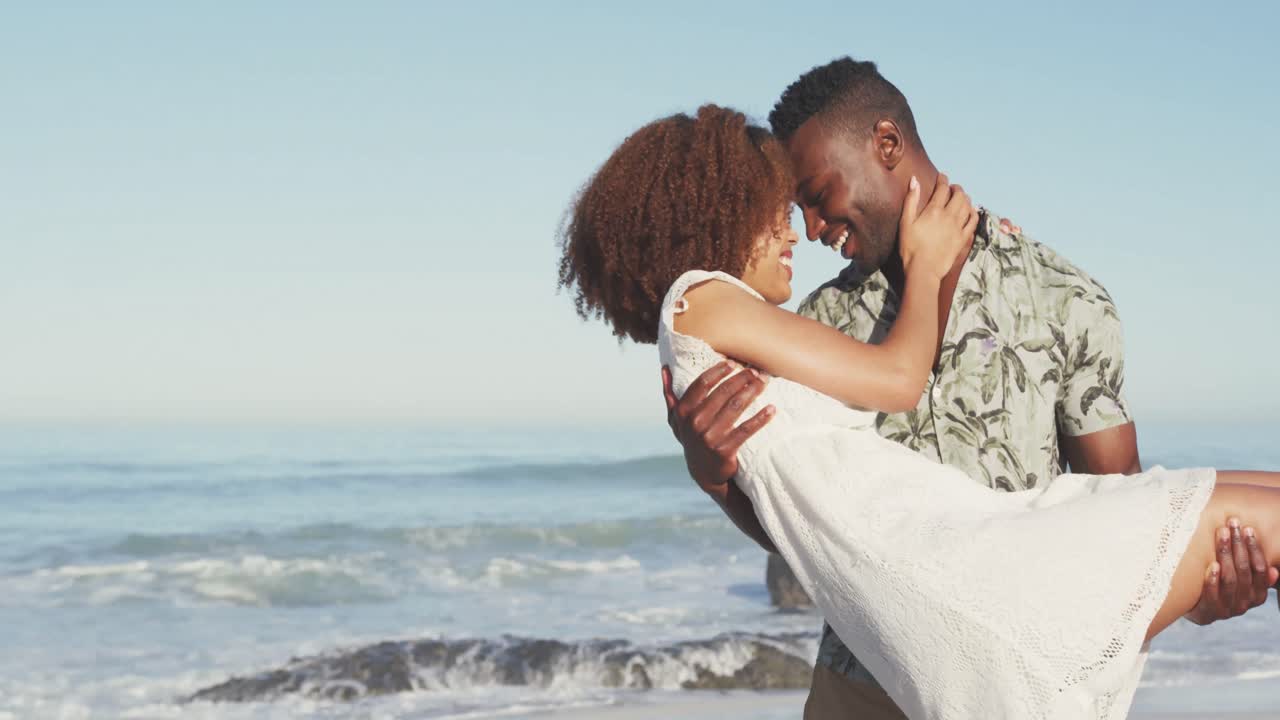 hombre afroamericano sosteniendo a su esposa en la playa