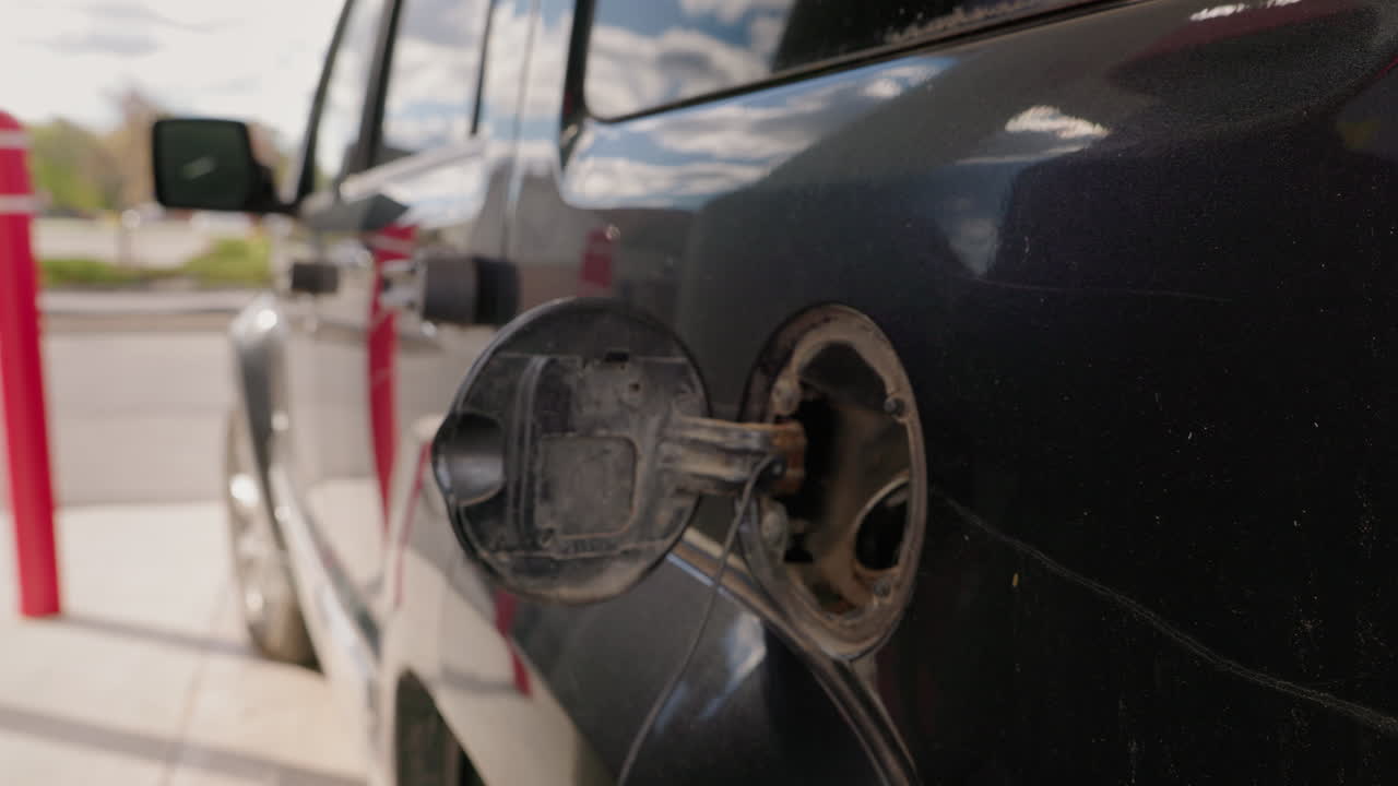 Bilist åbner tankdæksel og indsætter benzinpistol i bilen på tankstationen.