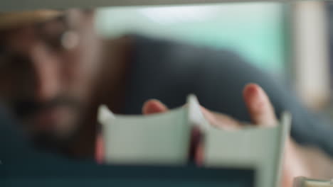 Primer plano en una biblioteca donde se ve a un estudiante ligeramente borroso deslizando la mano por encima de los libros en una estantería, sintiendo los lomos con un movimiento suave, con un soñador fondo bokeh.