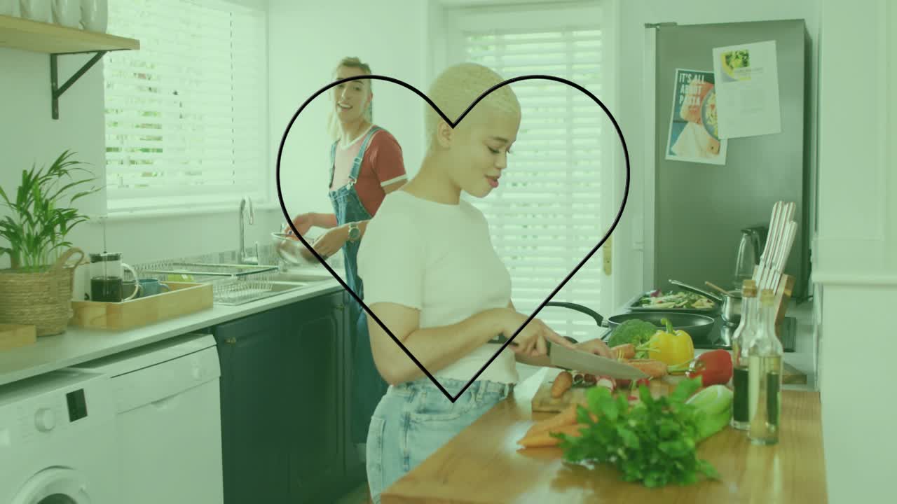 여자가 부엌에서 당근을 썰면서 건강을 위해 네온 하트 장식을 켜고, 파트너는 팬을 젓고 있어요.