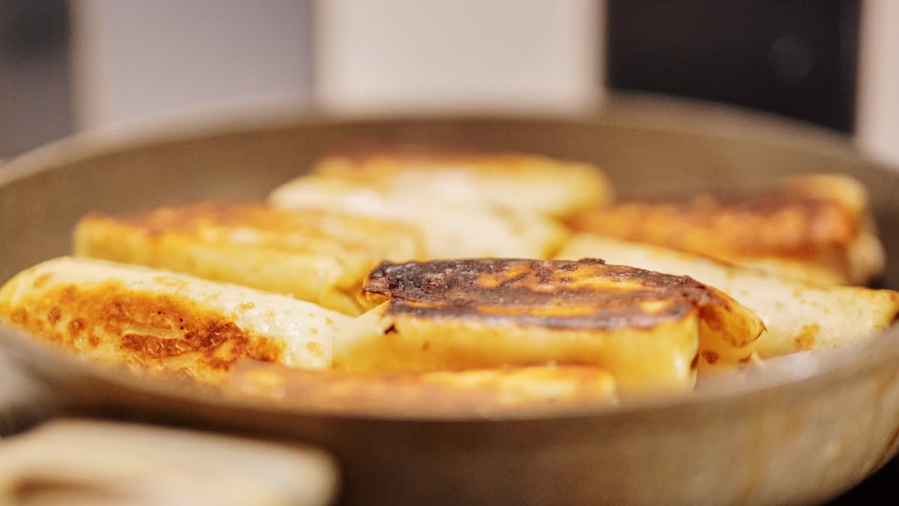 Close up of stuffed pancakes frying in pan with golden crust in warm kitchen