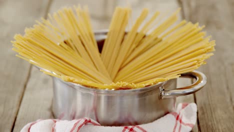 raw spaghetti arranged in silver pot places on red and white napkin on wooden table