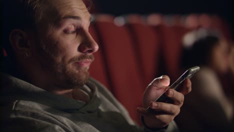 yawning man using smartphone in cinema. young man watching boring film