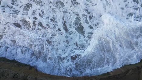 Drone-shot-straight-down-of-ocean-waves-washing-around-the-cliff-in-Carlsbad-California-during-high-tide