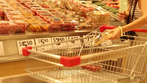 a person selects tomatoes in a well-lit supermarket aisle, placing them into a shopping cart