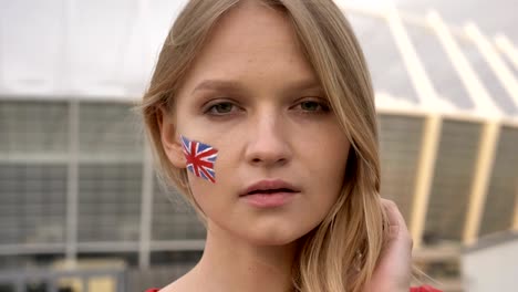 retrato de una joven rubia aficionada al fútbol de inglaterra mirando a la cámara, cara seria, estadio en el fondo 50 fps