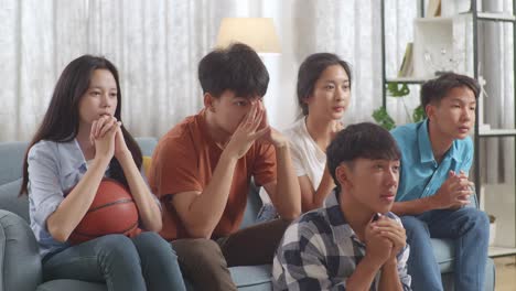 asian teenagers cheering and watching basketball game on tv and celebrating victory at home