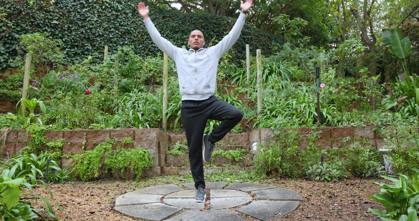 Starting from tree pose, man adjusting and keeping balance on stone platform in garden near bottle