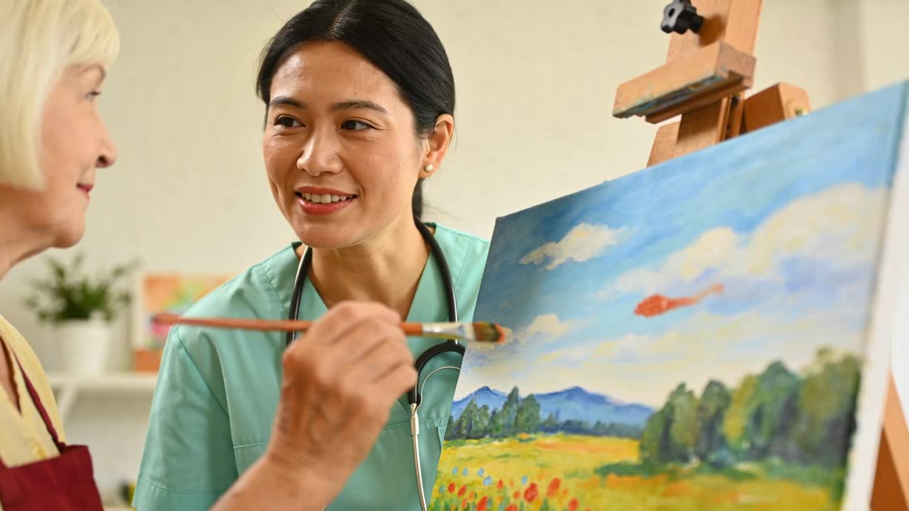 縦長動画：介護者の促しを受けて、高齢女性がオレンジ色の筆跡を描く療法を導く様子。