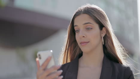 Cheerful-young-woman-using-smartphone-on-street