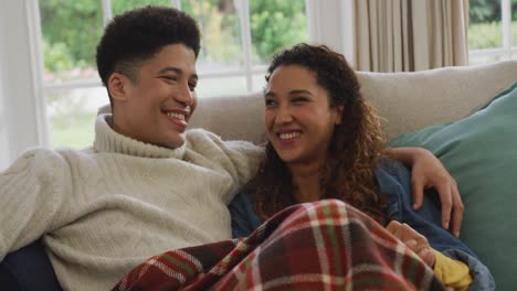 video of happy biracial couple siting on sofa under blanket