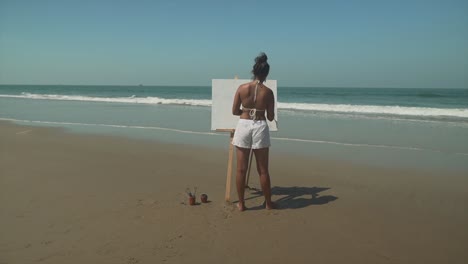 Cinematic-backshot,-a-young-female-is-painting-a-beautiful-canvas-at-a-sunny-beach