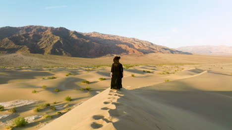 chica vestida de negro parada en las dunas de arena en el parque nacional del valle de la muerte