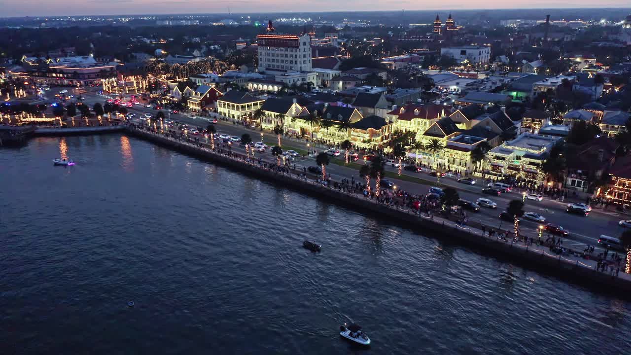 St. Augustine Night Of Lights havnefrontsgade oplyst af dekorative lys i aftentimerne, med både der sejler på roligt vand og en livlig atmosfære i et bymiljø