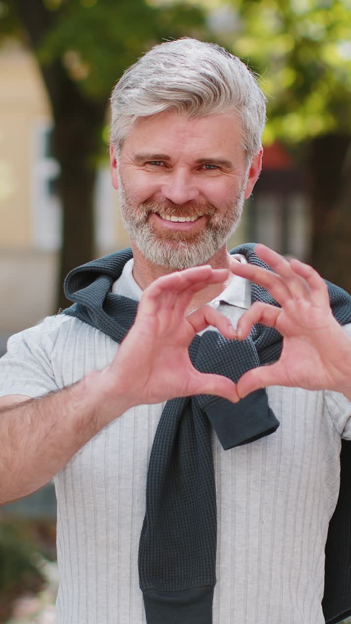성숙한 남자는 사랑의 상징으로 카메라에 심장 기호를 보여주며 만적 인 긍정적 인 감정을 표현합니다.