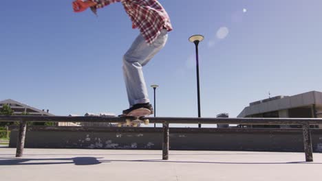 low section of caucasian man riding and jumping on skateboard on sunny day