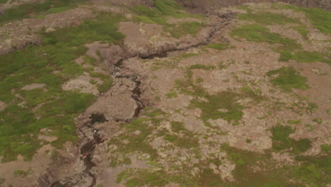 Iceland's-west-fjord-hills-and-water-streams,-tilt-down-drone-shot