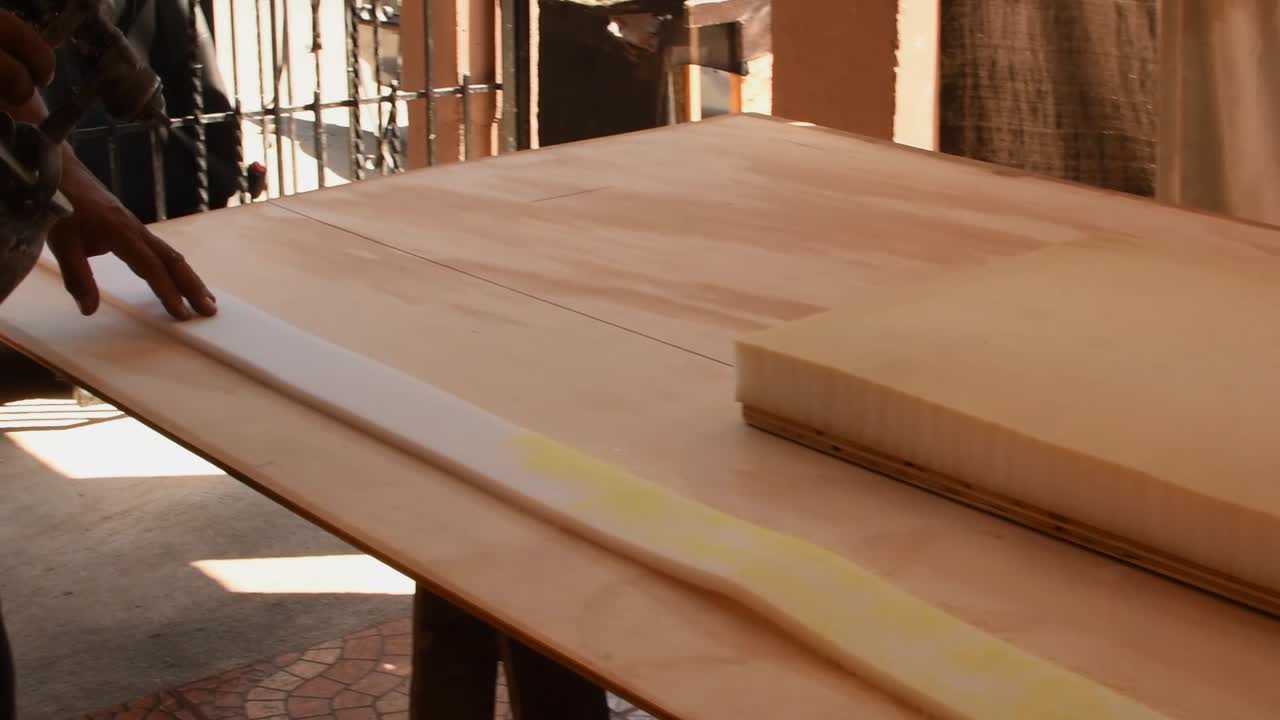 tapicero aplicando pegamento con una pistola pulverizadora para tapicería de esponjas en una mesa de madera -panorámica derecha