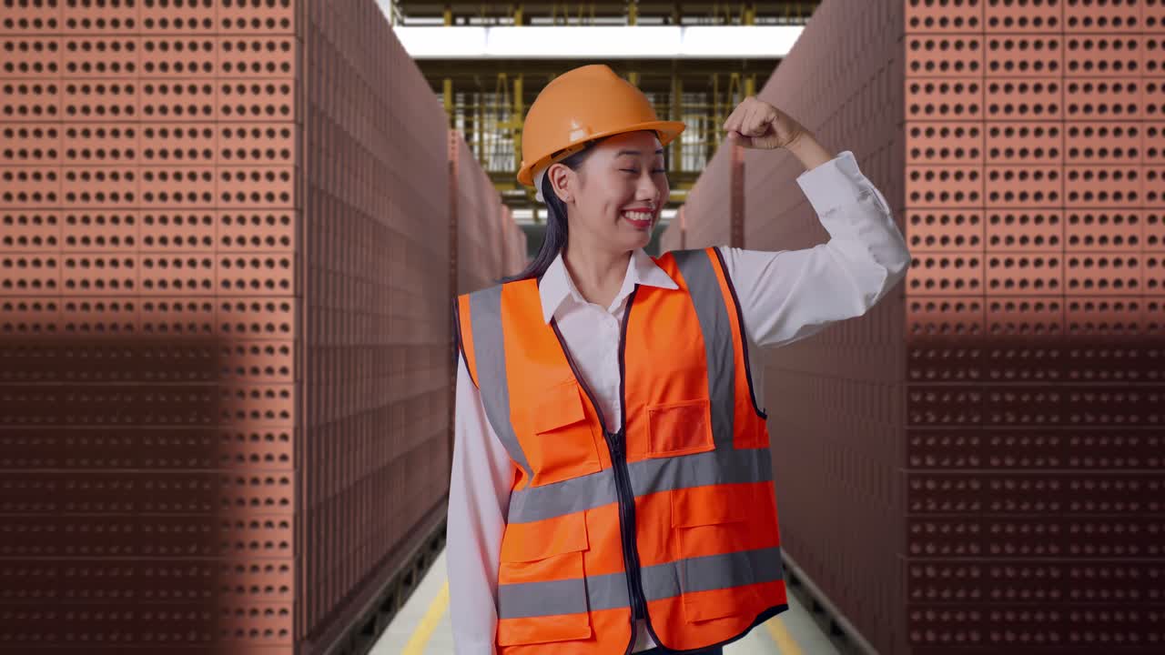 Asian Female Engineer With Safety Helmet Flexing Her Bicep And Smiling To Camera While Standing With Red Brick Packed in Stacks Are Stored