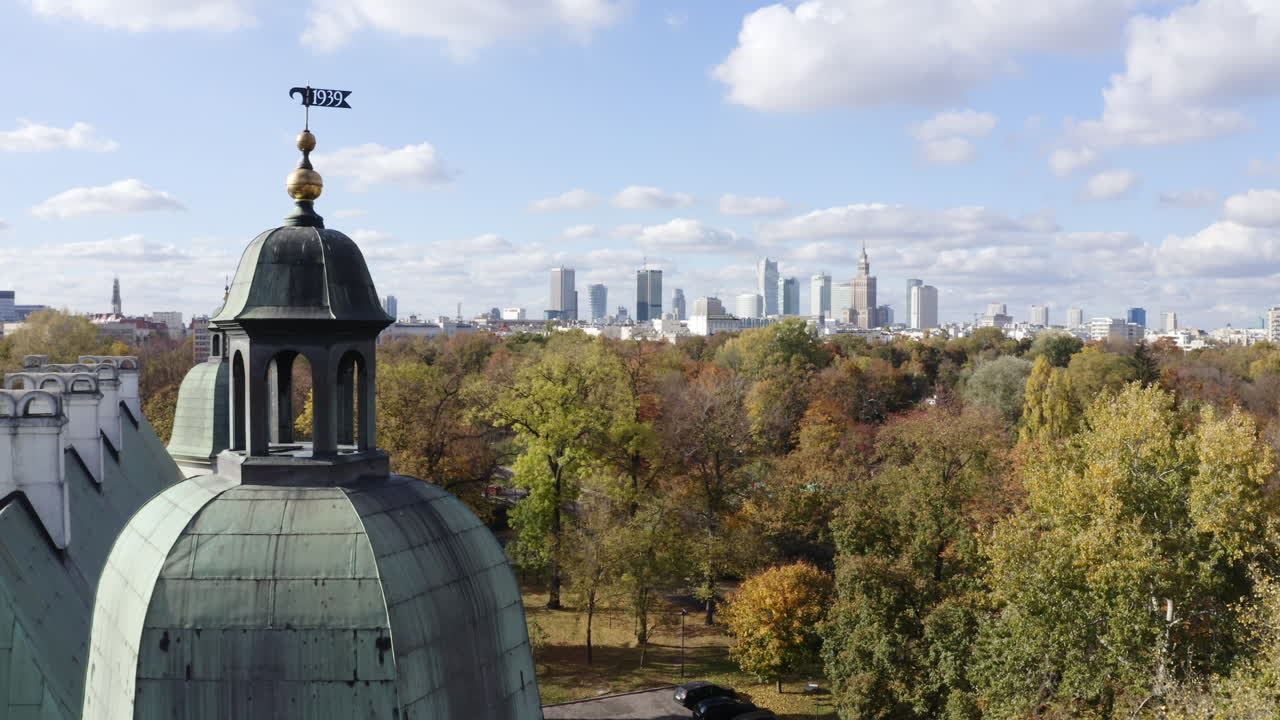 Drone rising over fall colored Łazienki Park, toward the skyline of Warsaw, Poland