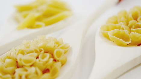 various pasta in wooden spoons on white background